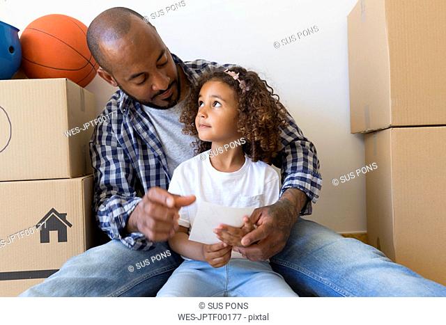 Father and daughter sitting on the floor at new home surrounded by cardboard boxes
