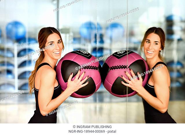 Woman lifting fitballs in the gym. Young girl wearing sportswear clothes in front of a mirror