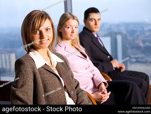 Group of People Looking at the Camera. Focus on first person's face. There's Big Window With Big City View Behind Them