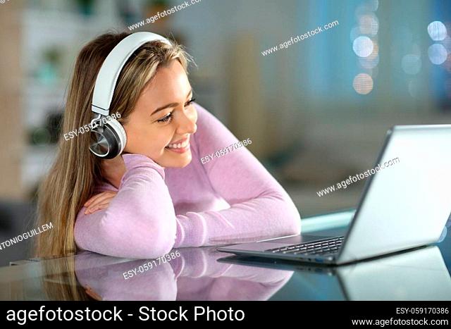 Happy teen watching videos on laptop in the night in the living room at home