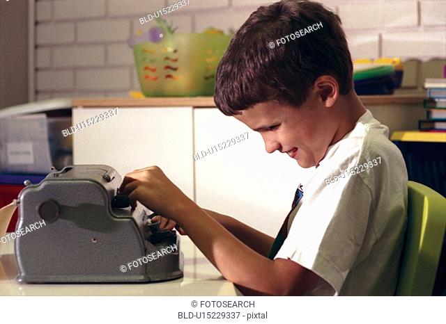 Cute little boy with multiple disabilities, including blindness, using a braille machine as he learns to type a letter
