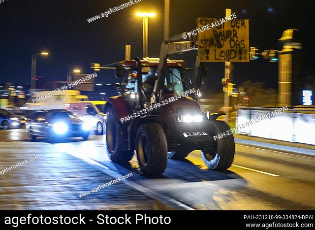 18 December 2023, Saxony, Leipzig: One of several farmers drives through the early morning rush hour traffic with his tractor and a protest poster