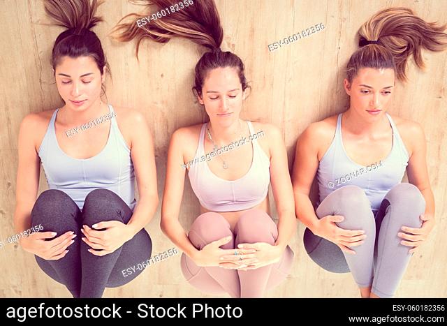 Group of three young sporty attractive women in yoga studio, lying on the floor, stretching and relaxing after the workout