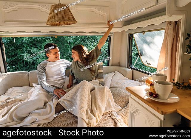 Smiling young man looking at girlfriend stretching while waking up in motor home