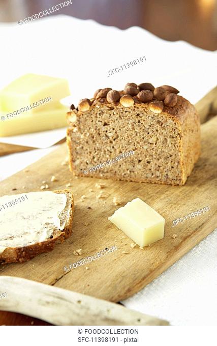 Sliced multigrain bread with almonds on a wooden board with a piece of cheese