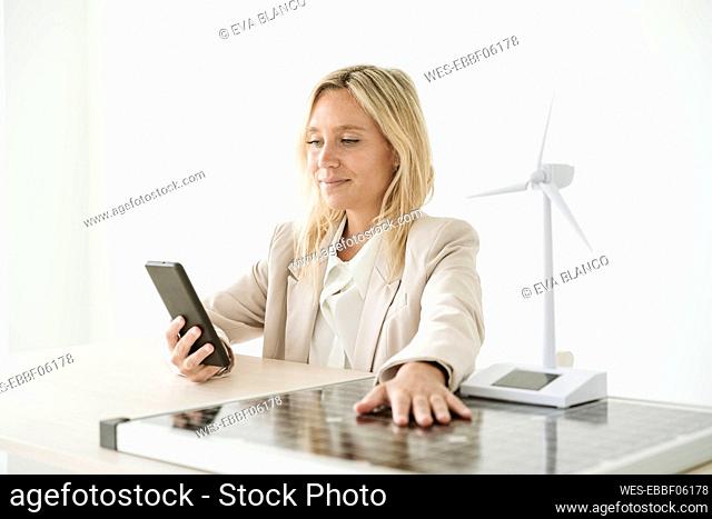 Woman using mobile phone with solar panel and wind turbine model on desk