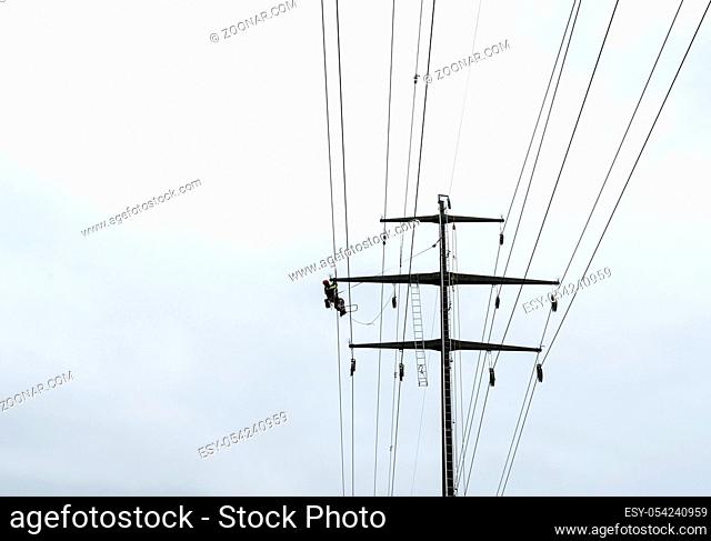 Working professional man on high voltage power lines high up on lattice crosses doing dangerous electrical work