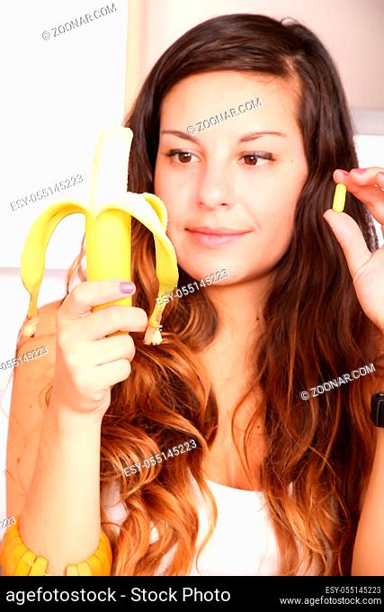 A young woman holding a supplement pill in one hand and a banana in the other