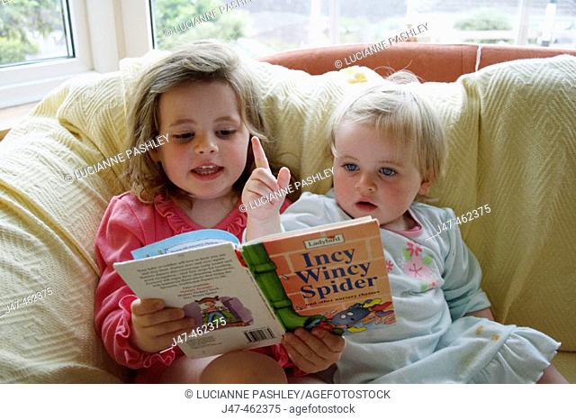 3 year old girl and 18 month old baby girl, sitting on the settee, reading a bedtime story