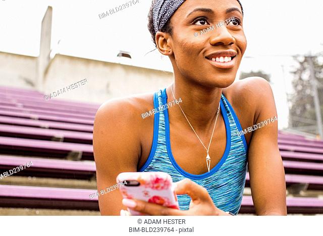 Smiling Black woman sitting on bleachers texting on cell phone