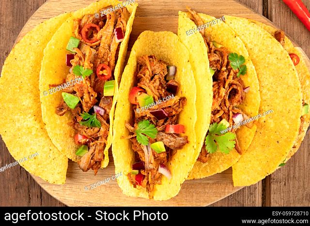 An overhead closeup photo of Mexican tacos with pulled meat, avocado, chili peppers, cilantro