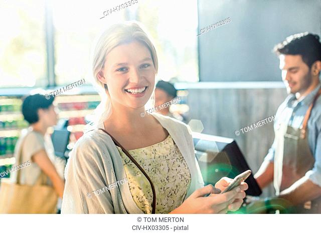 Portrait smiling young woman with cell phone at grocery store checkout