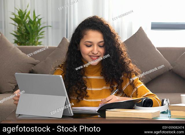 A TEENAGE GIRL HAPPILY SITIING AND STUDYING DURING ONLINE CLASS