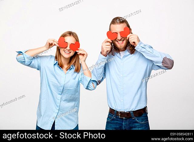 Attractive young in love couple holding red hearts over eyes on white background