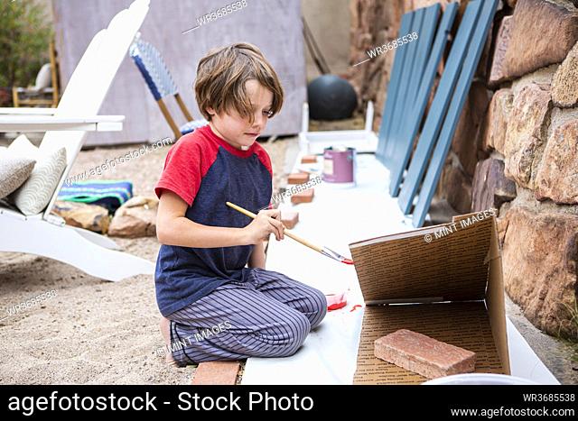 Seven year old boy using a paintbrush, painting cardboard