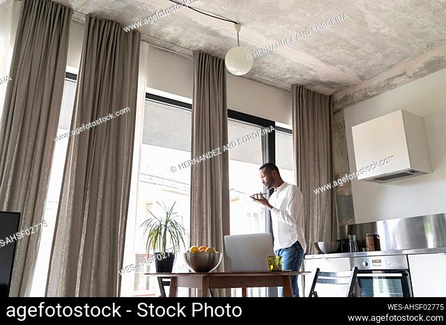 Man standing at Frencch door in modern apartment using smartphone