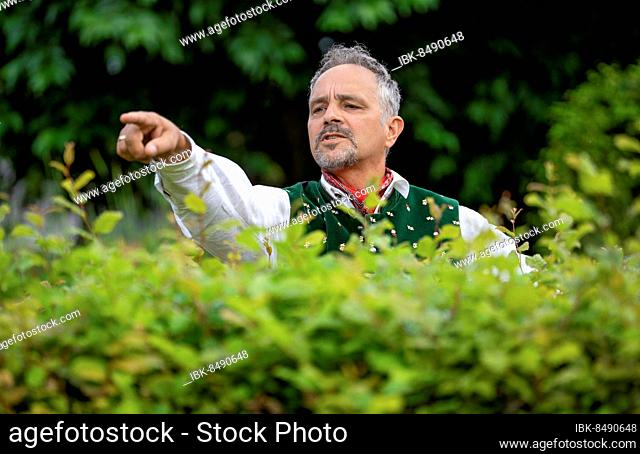 Neighbour in Bavarian traditional traditional costume points with hand over hedge, Karlsruhe, Germany, Europe