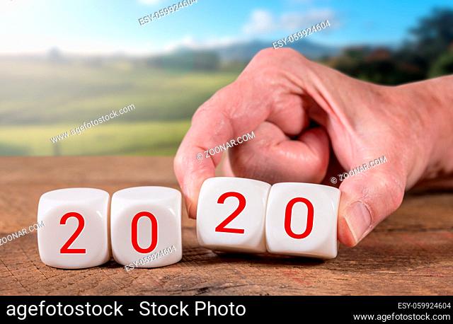2020 spelled in cubes with man's hand turns over the dice on wooden table with sunlight on rural landscape