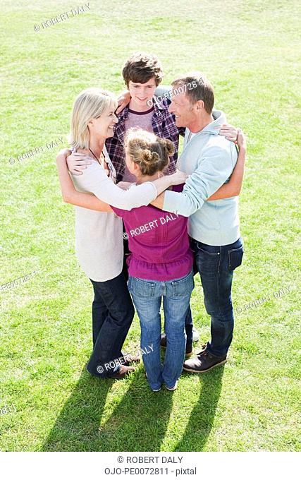 Smiling family hugging in a circle on grass