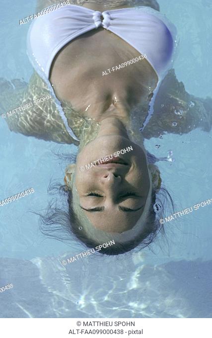 Young woman floating in swimming pool, eyes closed
