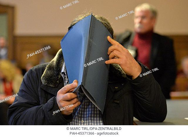 Talip M., taxi driver being charged with fraud, holds a folder up to his face in a courtroom in the Tiergarten regional court in Berlin, Germany