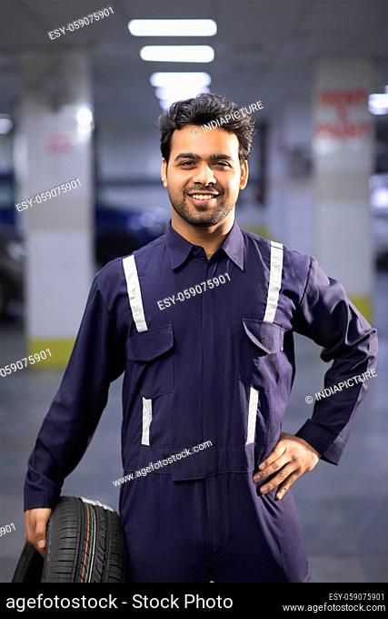 Portrait of smiling mechanic holding a tyre in auto repair shop
