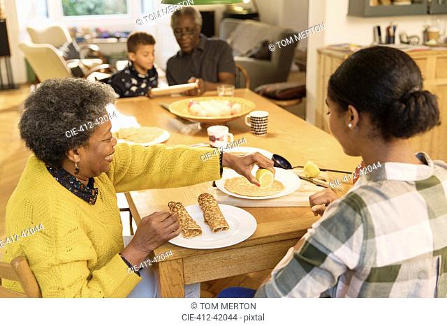 Grandmother and granddaughter eating crepes at dining table
