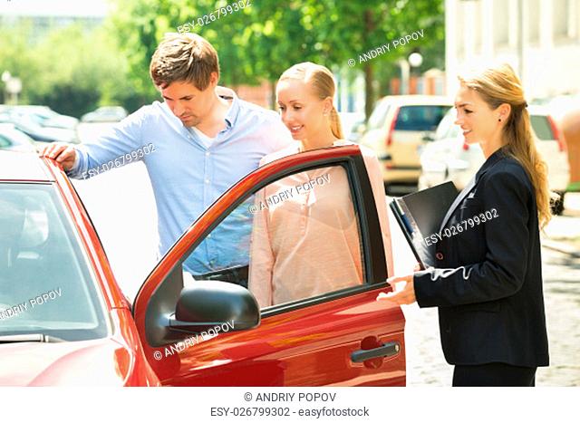 Saleswoman Standing Besides Couple Looking At New Red Car