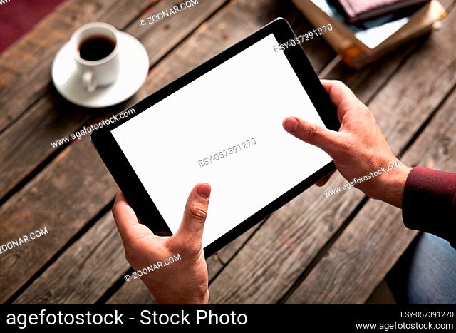 Tablet computer with isolated screen in male hands over cafe background - table, cup of coffee..