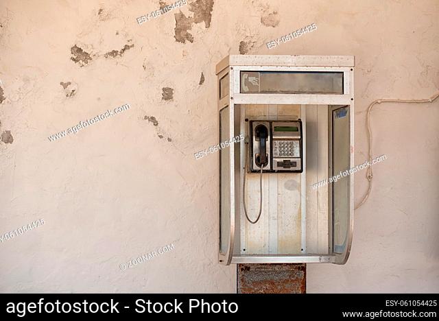Vintage pay public use phone cabin with metallic button phone on white ragged wall