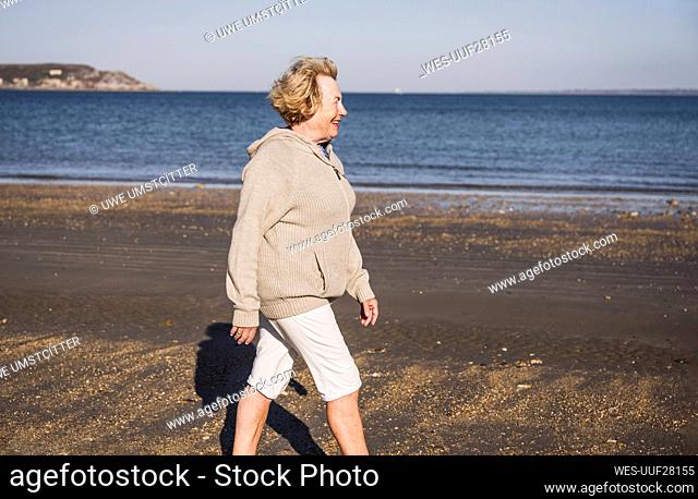 Smiling elderly woman walking by sea at beach