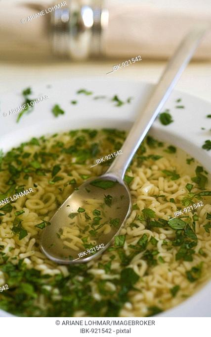 Alphabet soup with parsley and noodle letters, a spoon and a serviette in a serviette ring