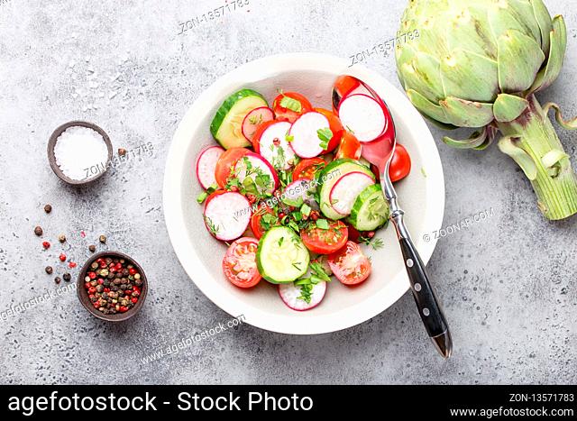 Close-up of fresh healthy salad in a bowl made of tomatoes, cucumber, radish and herbs, with raw artichoke and seasonings, good for diet or detox