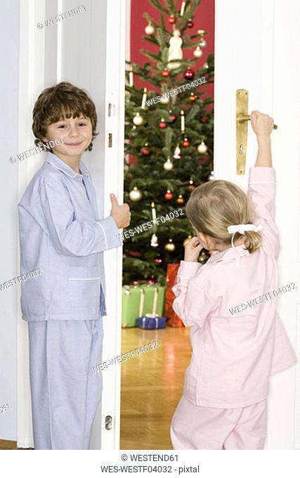 Girl and boy standing at door watching Christmas tree