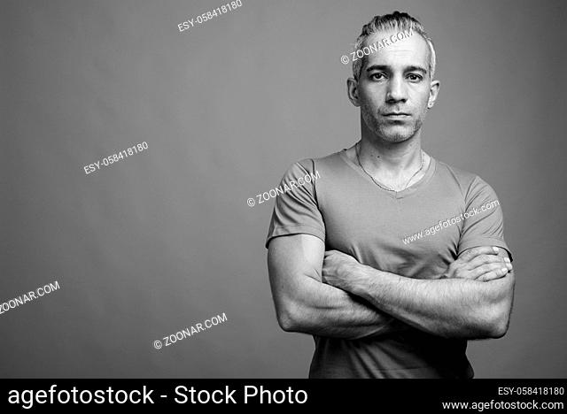 Studio shot of handsome Persian man with gray hair against gray background in black and white