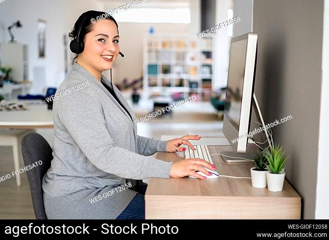 Smiling female customer service representative using computer while working at home office