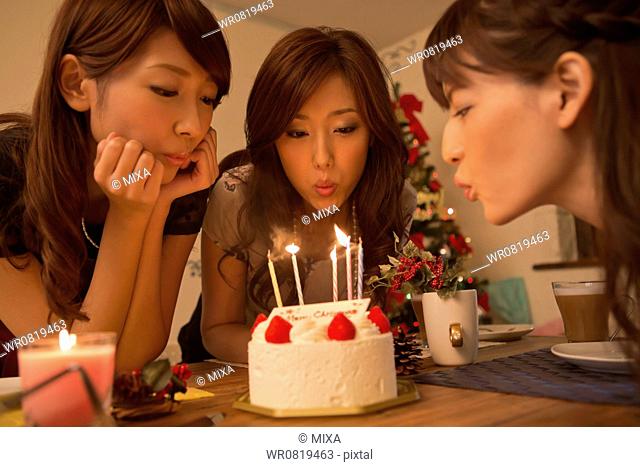 Three Young Women Blowing Out Candles on Christmas Cake