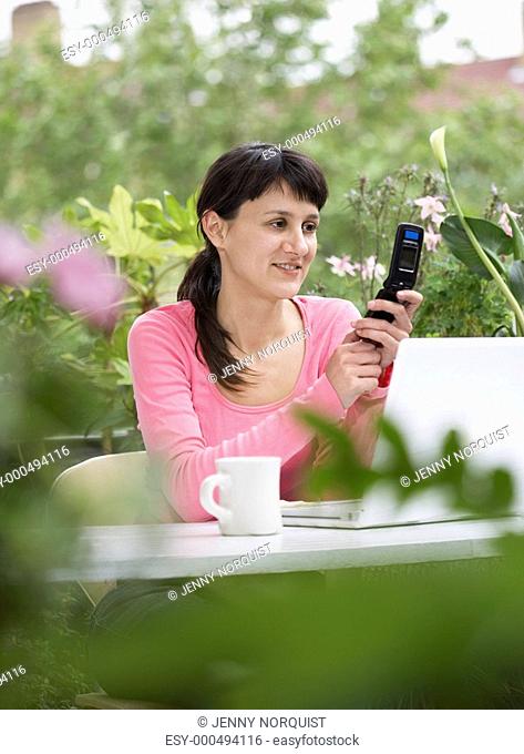 Businesswoman looking happily at Cell Phone with white laptop in garden