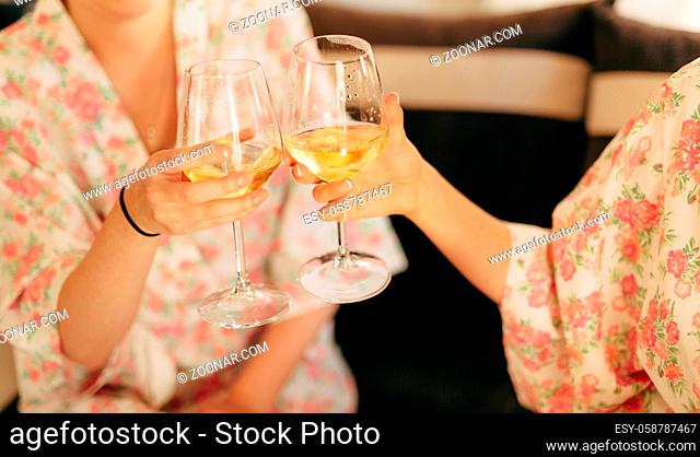 The girls clink glasses of champagne in robes