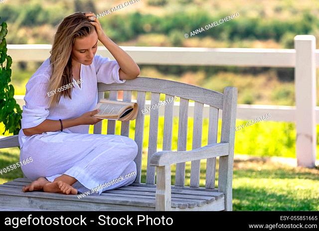 Beautiful Young Woman Sitting on the Bench in the Park and Reading a Book. Spending Nice Summer Day with Good Story. Peace and Relaxation Concept