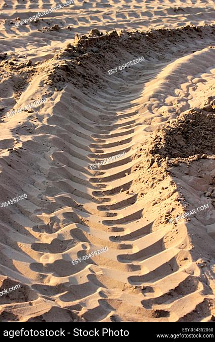Fresh tracks in sand of a heavy construction vehicle are run into the distance. Tire tracks of a large vehicle in sand on a building area to road