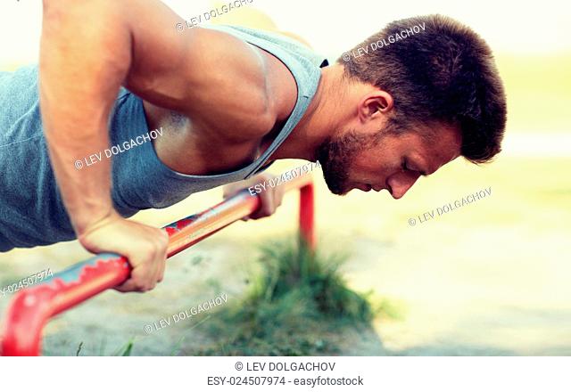 fitness, sport, exercising, training and lifestyle concept - young man doing push ups on horizontal bar outdoors