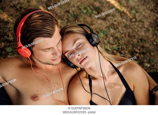 Young couple lying on grass, listening music with headphones