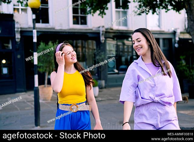 Smiling woman walking by friend with hand in hair