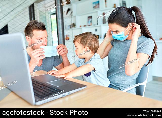 Eltern und Kind mit Mund-Nasen-Schutz am Laptop Computer wegen Coronavirus