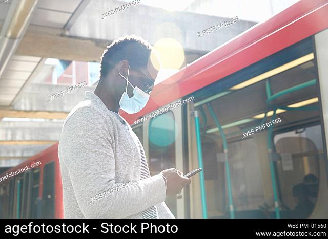 Businessman wearing protective face mask while using mobile phone at railroad station