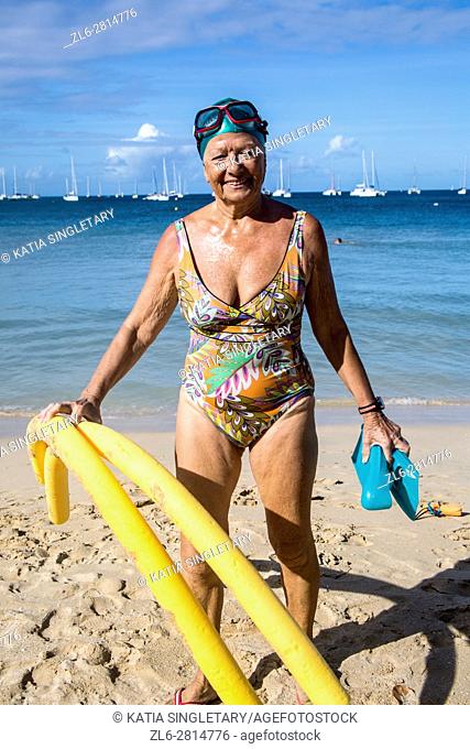 Senior retired caucasian woman, in her 70's, with her swim cap, flippers and goggles, going to the ocean doing her exercices to stay fit