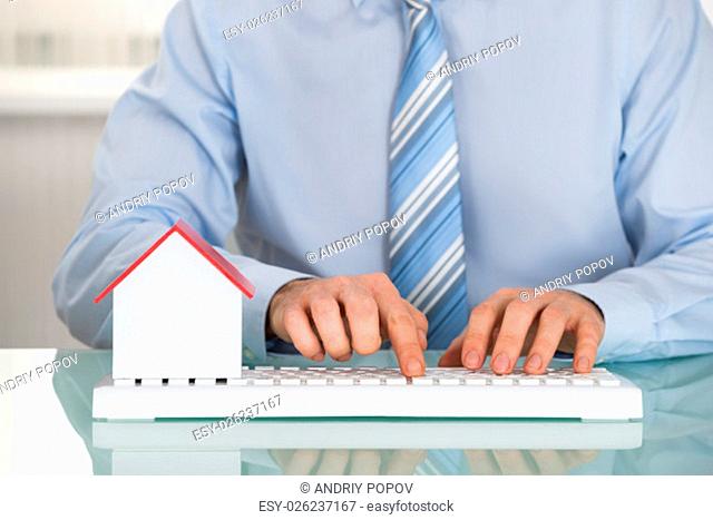 Close-up Of A Businessman With House Model Using Keyboard