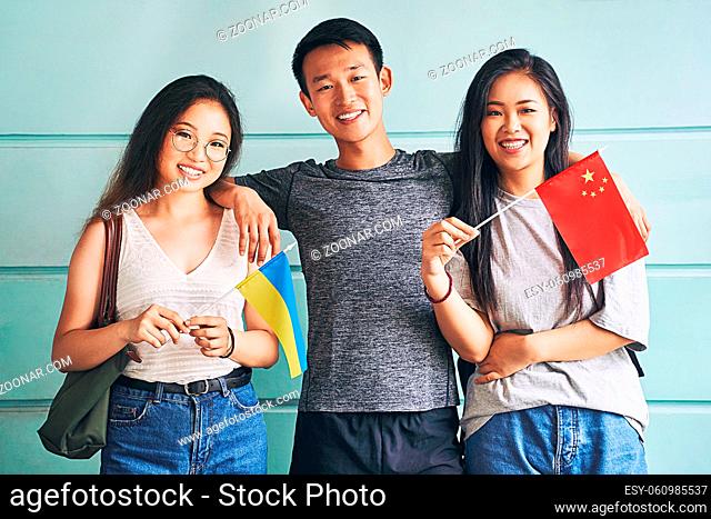 Group of three international chinese asian students smiling and holding flags of China and Ukraine in university
