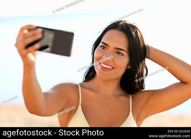 smiling woman in bikini taking selfie on beach